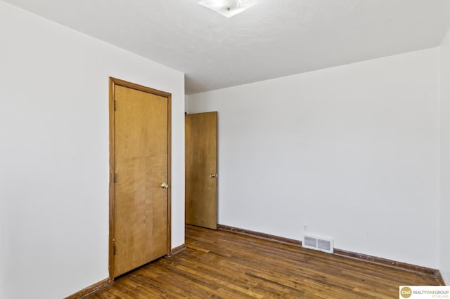 unfurnished room with dark wood-style floors, visible vents, and baseboards