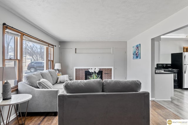 living area featuring a textured ceiling, light wood-type flooring, and a brick fireplace