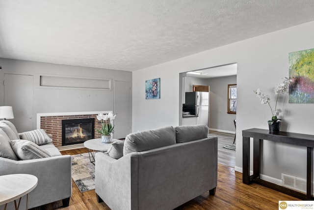 living area featuring a fireplace, visible vents, dark wood-type flooring, a textured ceiling, and baseboards