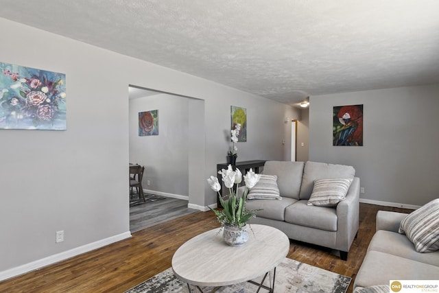 living area with a textured ceiling, dark wood-type flooring, and baseboards