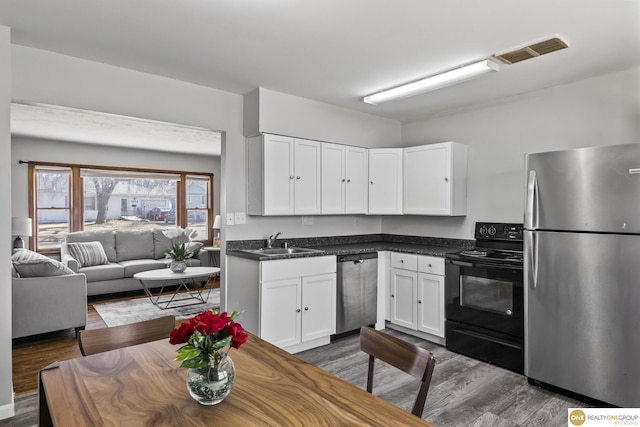 kitchen featuring dark countertops, visible vents, appliances with stainless steel finishes, open floor plan, and white cabinetry