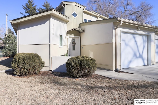 view of side of property featuring a garage, concrete driveway, and stucco siding