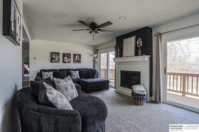 living area with carpet floors, a textured ceiling, a fireplace, and a ceiling fan