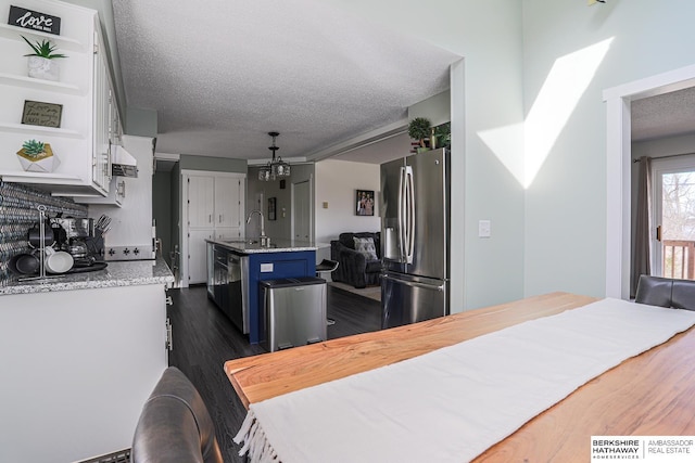 kitchen featuring light stone counters, blue cabinets, stainless steel refrigerator with ice dispenser, open shelves, and an island with sink