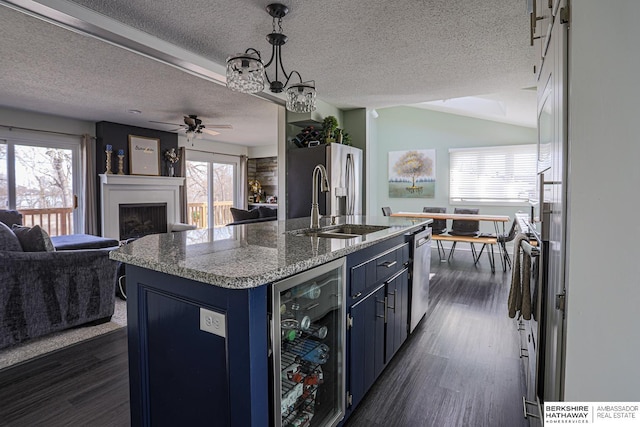 kitchen with beverage cooler, a fireplace, open floor plan, blue cabinetry, and a center island with sink