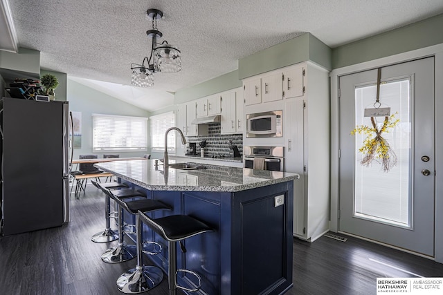 kitchen with a sink, white cabinets, appliances with stainless steel finishes, dark stone countertops, and decorative light fixtures