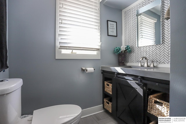 half bath featuring decorative backsplash, baseboards, a sink, and toilet