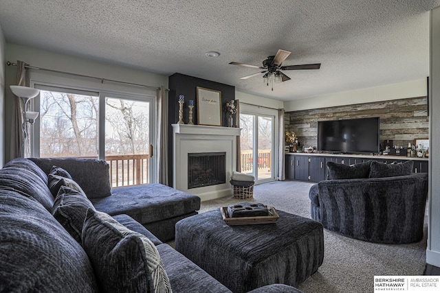 living room featuring a fireplace with raised hearth, a ceiling fan, carpet, a textured ceiling, and wood walls