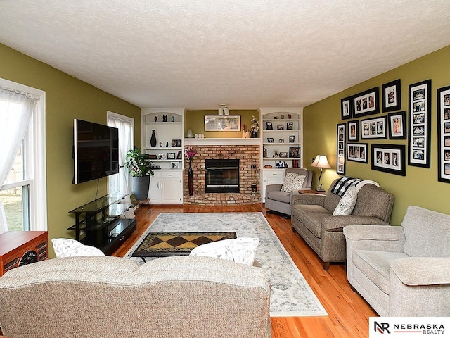 living room featuring a textured ceiling, built in shelves, a fireplace, and wood finished floors