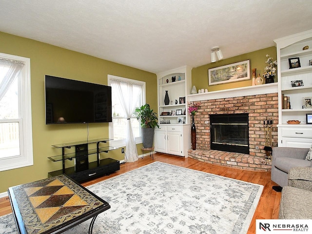 living area featuring built in features, a brick fireplace, a textured ceiling, wood finished floors, and baseboards