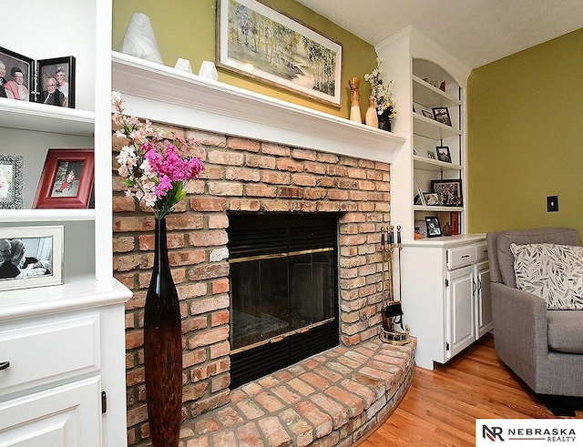 living room featuring light wood-style floors, a brick fireplace, and built in shelves