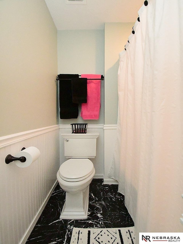 bathroom featuring marble finish floor, a wainscoted wall, and toilet