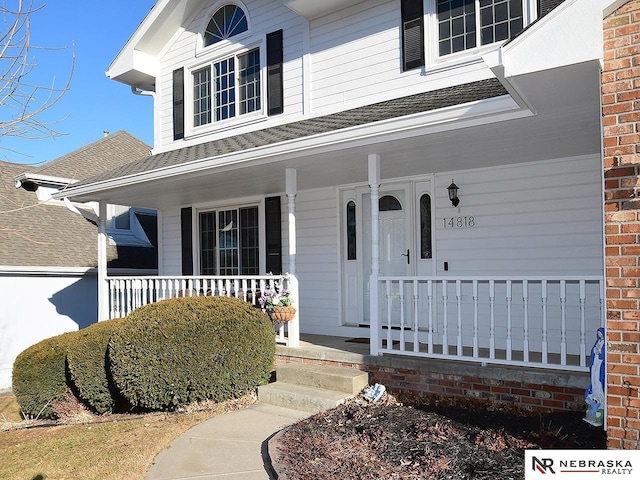 property entrance with a shingled roof, covered porch, and brick siding