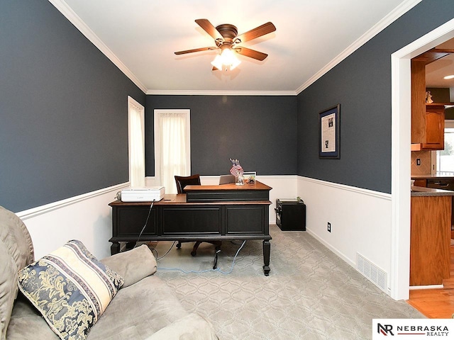 home office featuring a wainscoted wall, ornamental molding, visible vents, and a ceiling fan