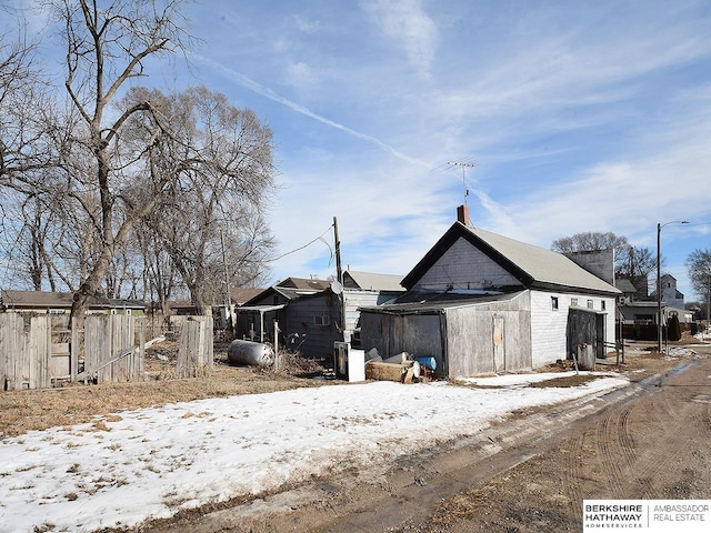 view of snowy exterior featuring an outbuilding and fence