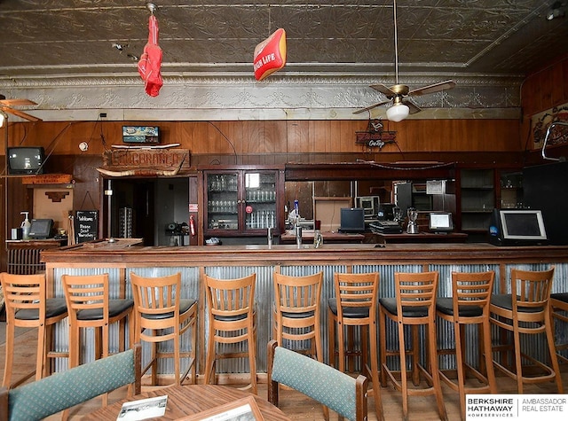 bar featuring a bar, wood walls, an ornate ceiling, and ceiling fan