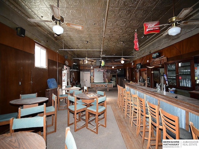 dining area with a dry bar, wood walls, an ornate ceiling, and a ceiling fan