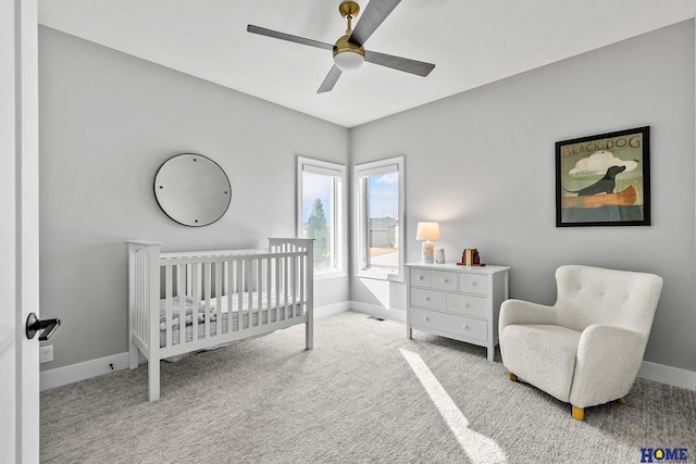 bedroom with a ceiling fan, light carpet, a crib, and baseboards