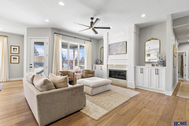 living area featuring baseboards, recessed lighting, a tiled fireplace, and light wood-style floors