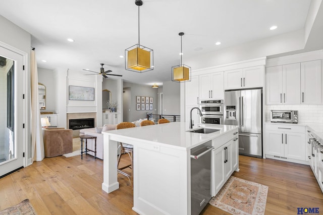 kitchen with a kitchen island with sink, stainless steel appliances, white cabinets, light countertops, and pendant lighting