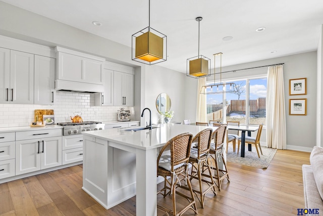 kitchen featuring pendant lighting, stainless steel gas cooktop, a center island with sink, white cabinetry, and a sink