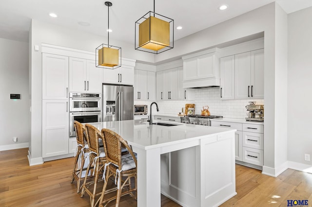 kitchen featuring stainless steel appliances, light countertops, a center island with sink, and decorative light fixtures