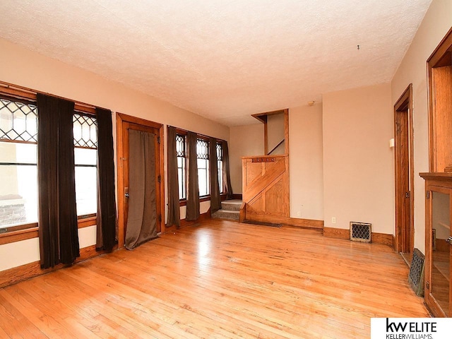 unfurnished living room featuring light wood finished floors, a wealth of natural light, and visible vents