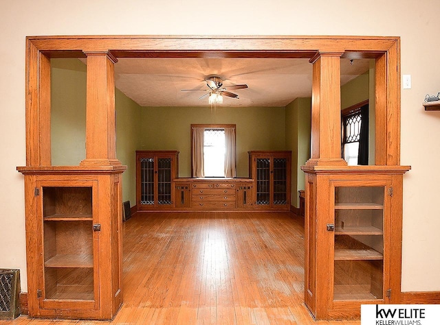 unfurnished living room with wood-type flooring, a ceiling fan, and ornate columns