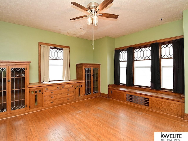 interior space with baseboards, visible vents, a ceiling fan, hardwood / wood-style floors, and a textured ceiling