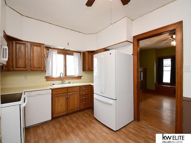 kitchen with light wood finished floors, white appliances, a sink, and brown cabinets