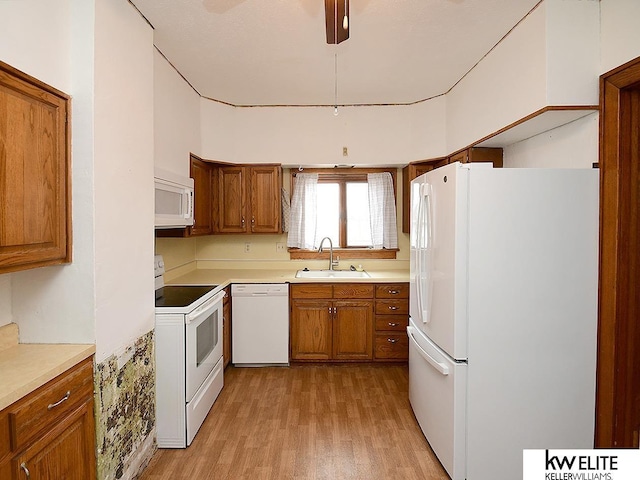 kitchen featuring brown cabinetry, white appliances, a sink, and light wood-style flooring