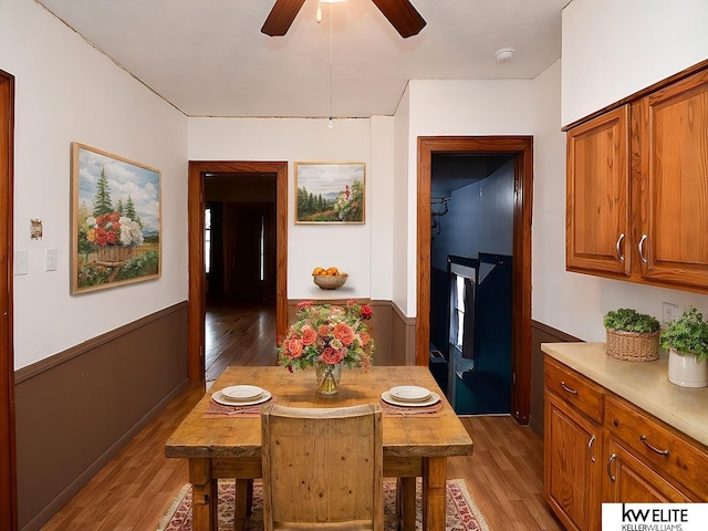 dining room featuring a ceiling fan, a wainscoted wall, and light wood-style flooring