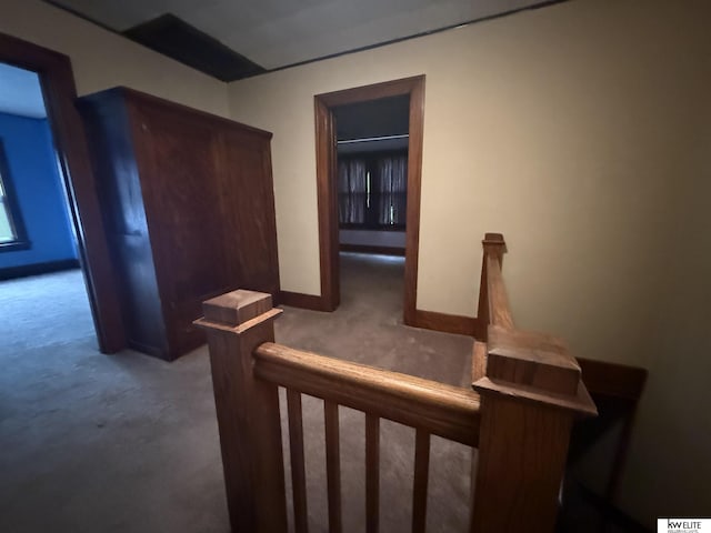 hallway featuring carpet flooring, an upstairs landing, and baseboards