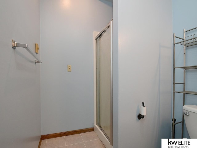 bathroom with toilet, a stall shower, baseboards, and tile patterned floors