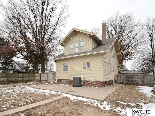 snow covered house with central AC unit, a chimney, and a fenced backyard