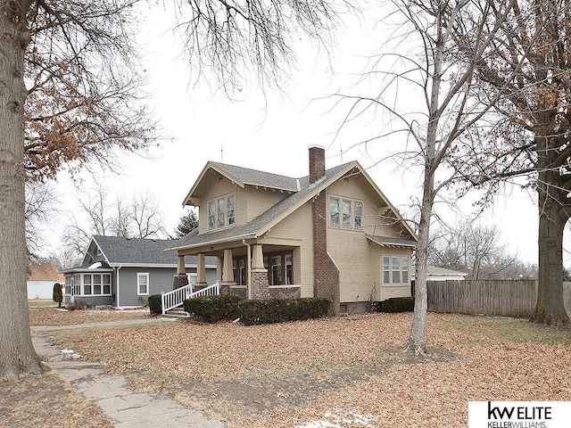 view of front facade featuring covered porch, brick siding, fence, and a chimney