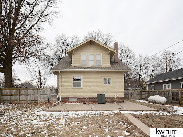 snow covered rear of property featuring a patio area, a fenced backyard, a chimney, and cooling unit