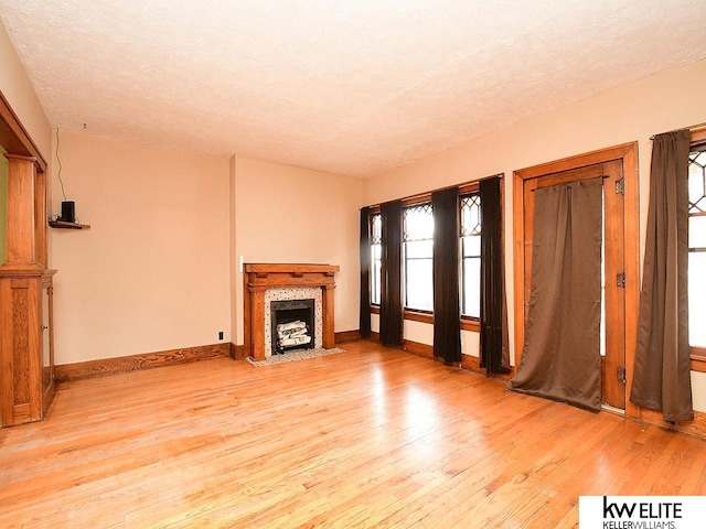 unfurnished living room featuring light wood finished floors, a fireplace with flush hearth, baseboards, and a textured ceiling