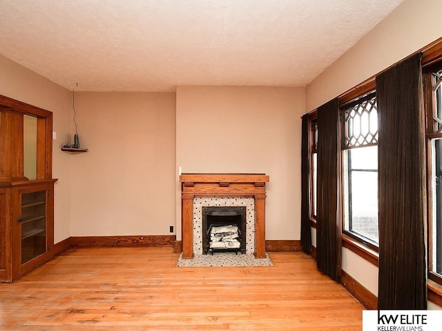 unfurnished living room featuring light wood-style floors, baseboards, and a tiled fireplace