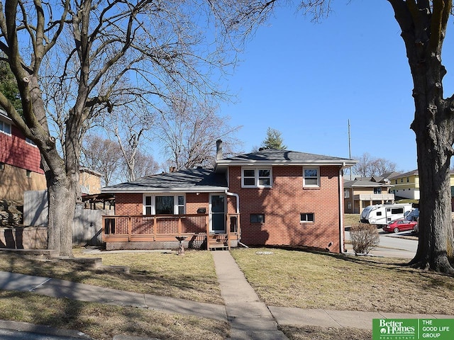 tri-level home featuring brick siding, a wooden deck, and a front lawn