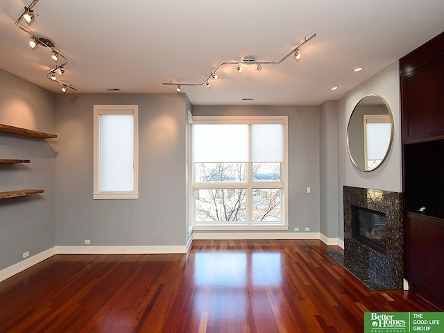 unfurnished living room with dark wood-type flooring, track lighting, a tiled fireplace, and baseboards