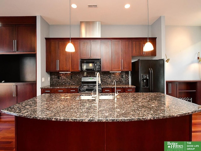 kitchen with wood finished floors, visible vents, backsplash, black appliances, and a center island with sink