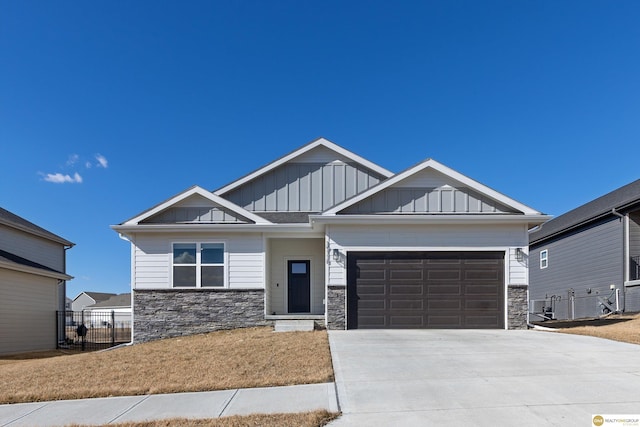 craftsman-style home with a garage, concrete driveway, stone siding, fence, and board and batten siding