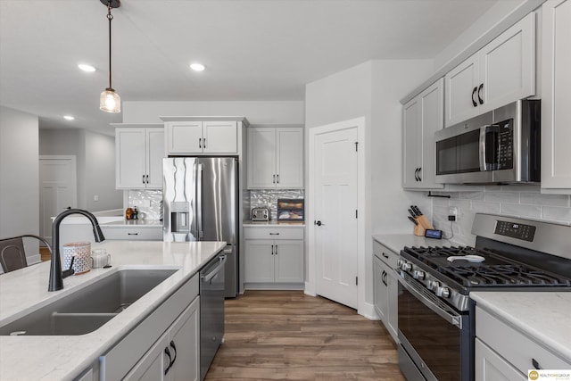 kitchen featuring recessed lighting, stainless steel appliances, wood finished floors, a sink, and hanging light fixtures