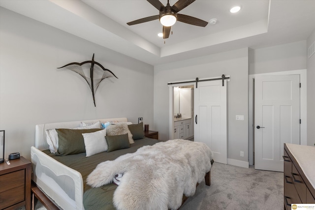 bedroom with a raised ceiling, light colored carpet, baseboards, and a barn door