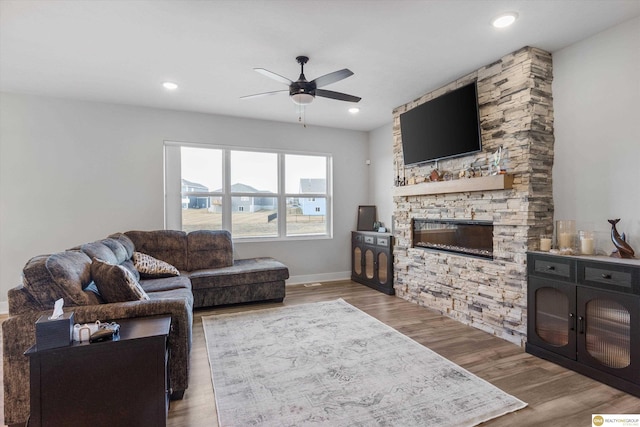 living room with a stone fireplace, wood finished floors, a ceiling fan, and recessed lighting