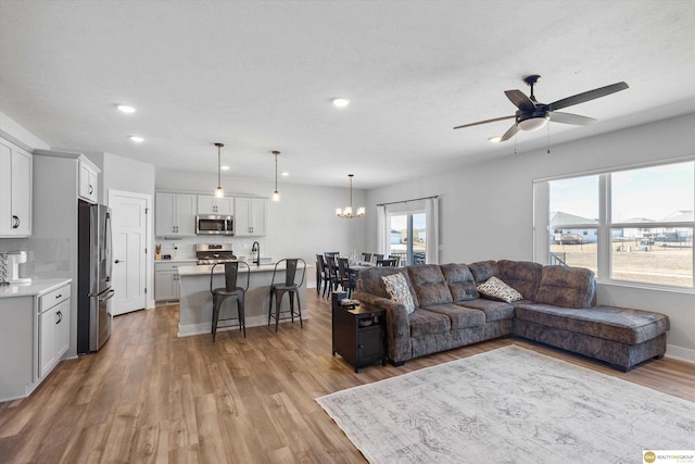 living room with baseboards, light wood-style flooring, ceiling fan with notable chandelier, a textured ceiling, and recessed lighting