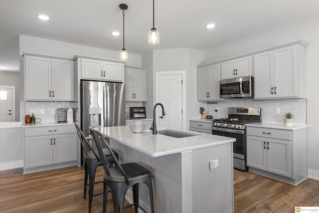 kitchen featuring dark wood-style floors, a breakfast bar area, decorative light fixtures, stainless steel appliances, and a sink