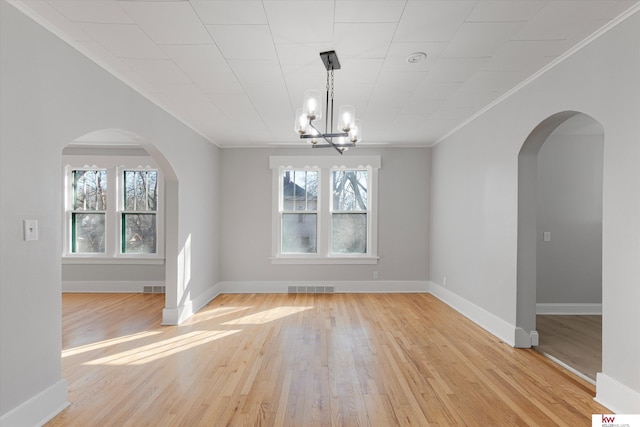 unfurnished dining area with arched walkways, crown molding, visible vents, light wood-type flooring, and baseboards