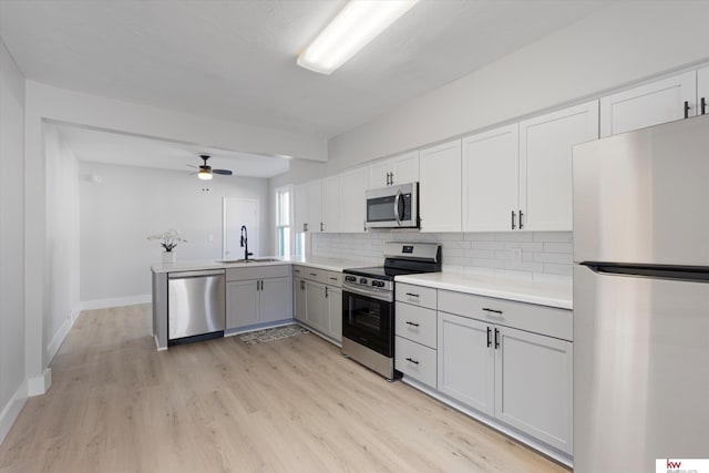 kitchen featuring light wood-style flooring, gray cabinetry, stainless steel appliances, a sink, and tasteful backsplash